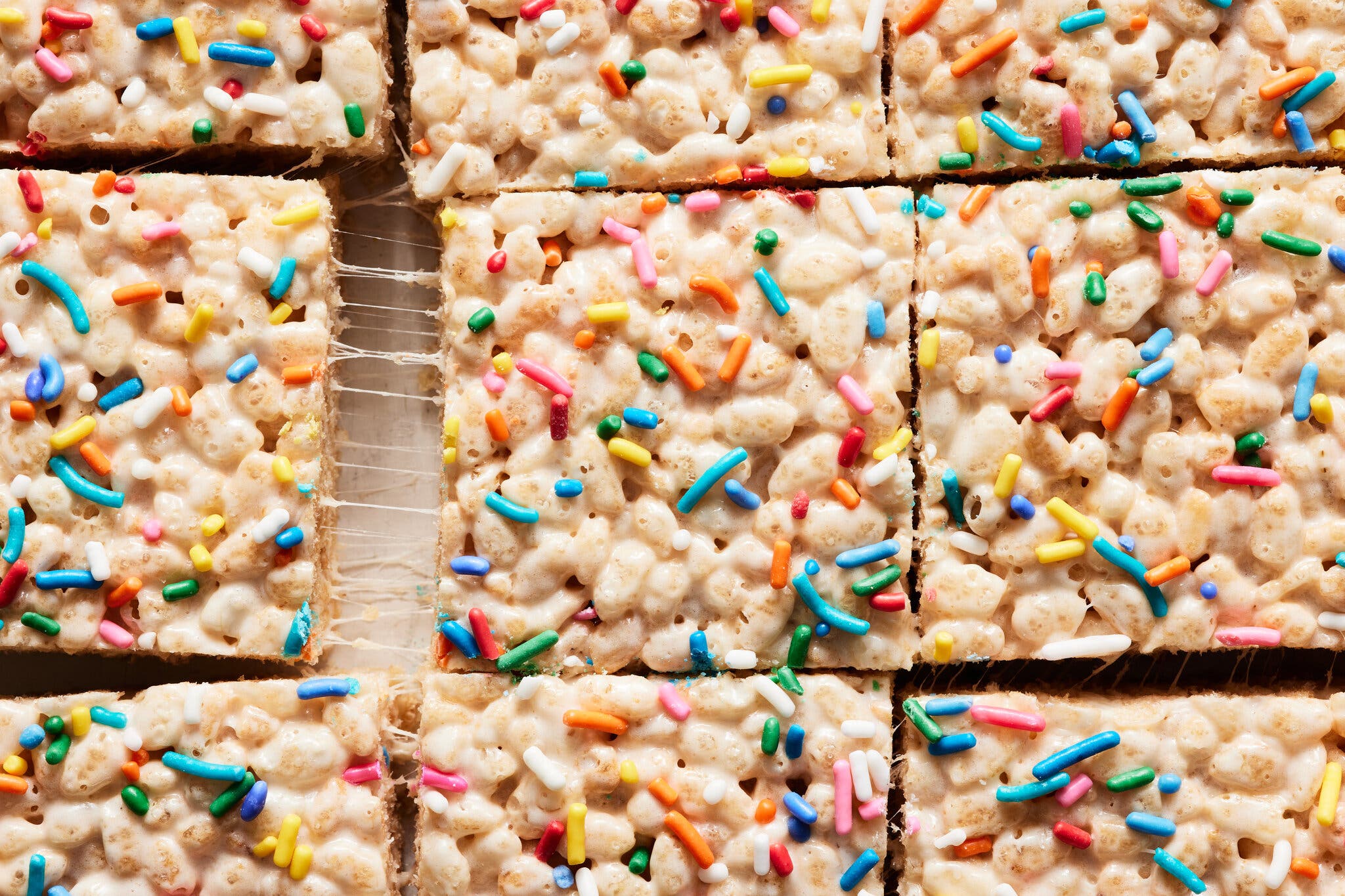 A pan of Rice Krispie treats topped with rainbow sprinkles cut into squares.