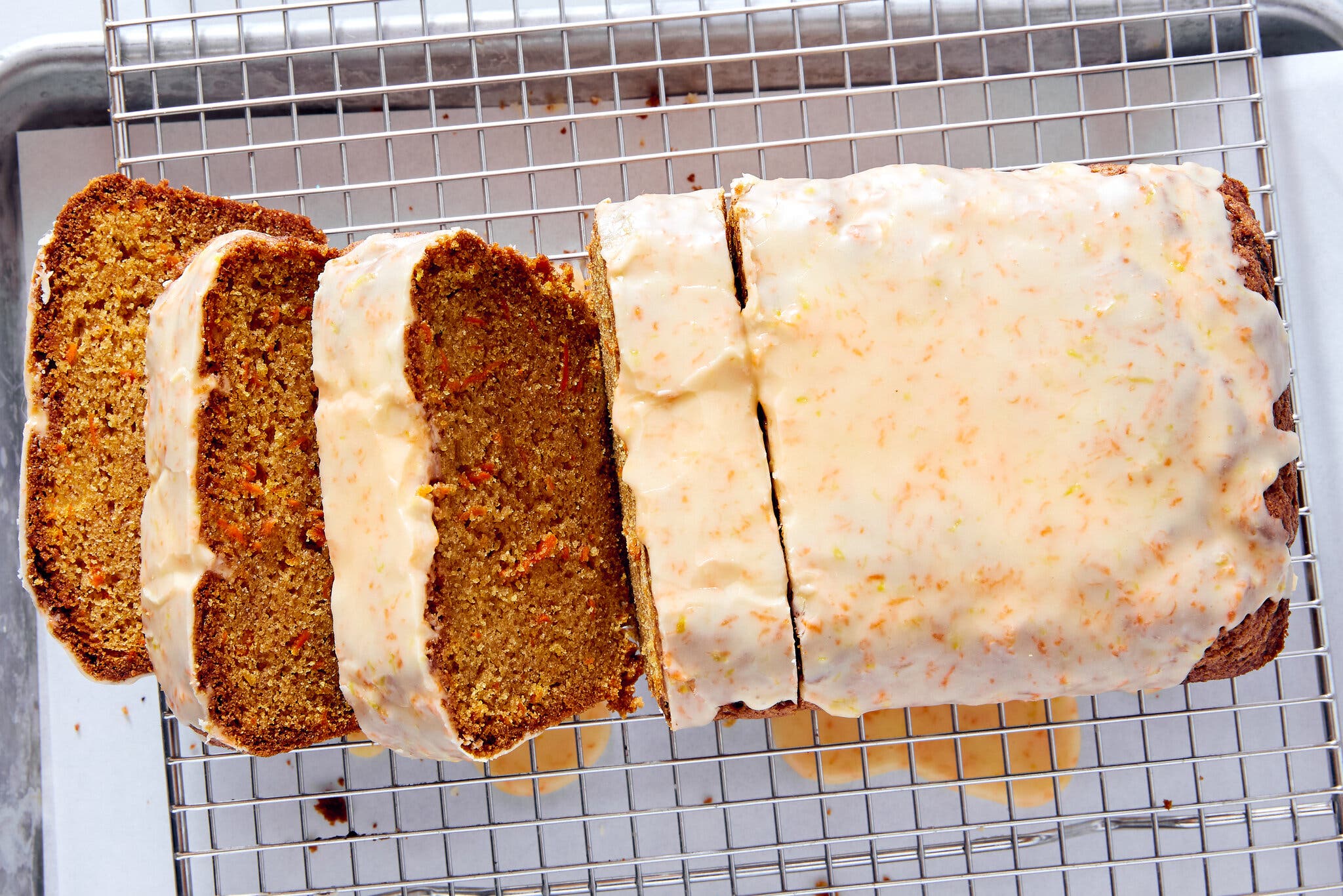 A glazed carrot loaf cake sliced on a wire rack over a baking sheet.