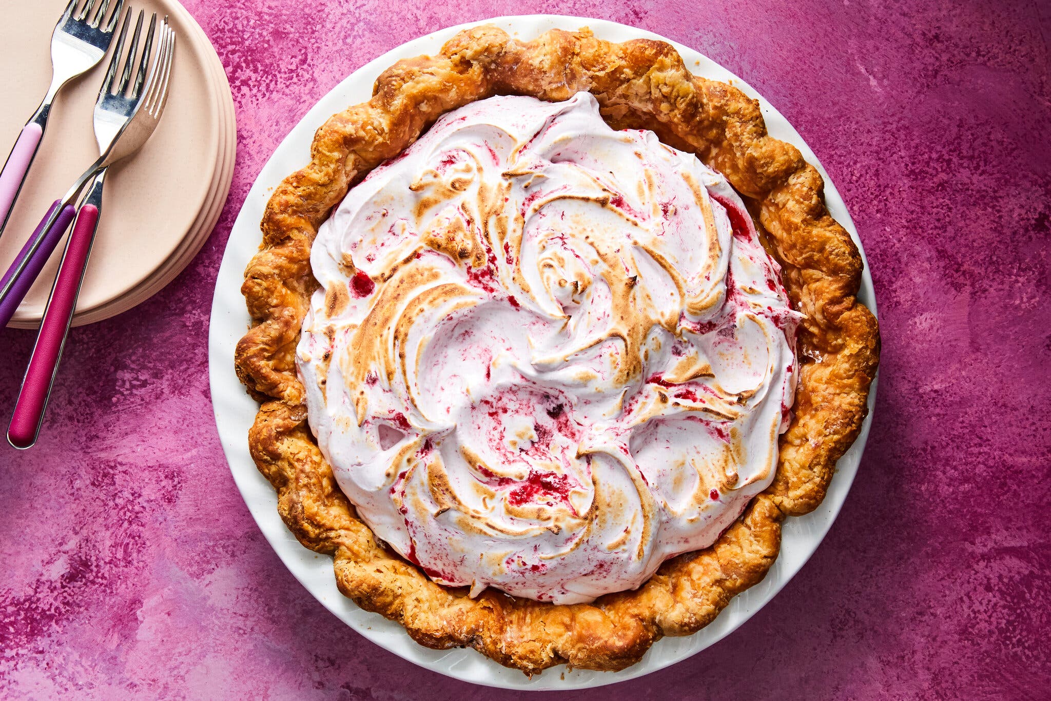 A meringue pie, swirled pink on top, sits on a dark pink surface.