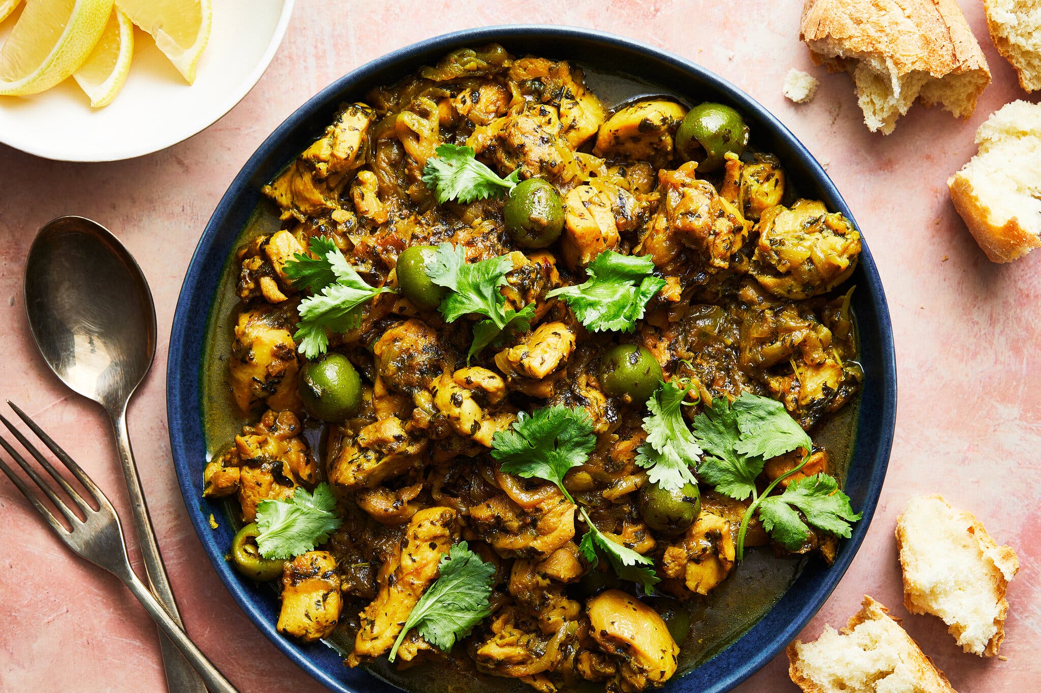 Chunks of chicken scattered with olives and herbs sit on a deep blue plate.