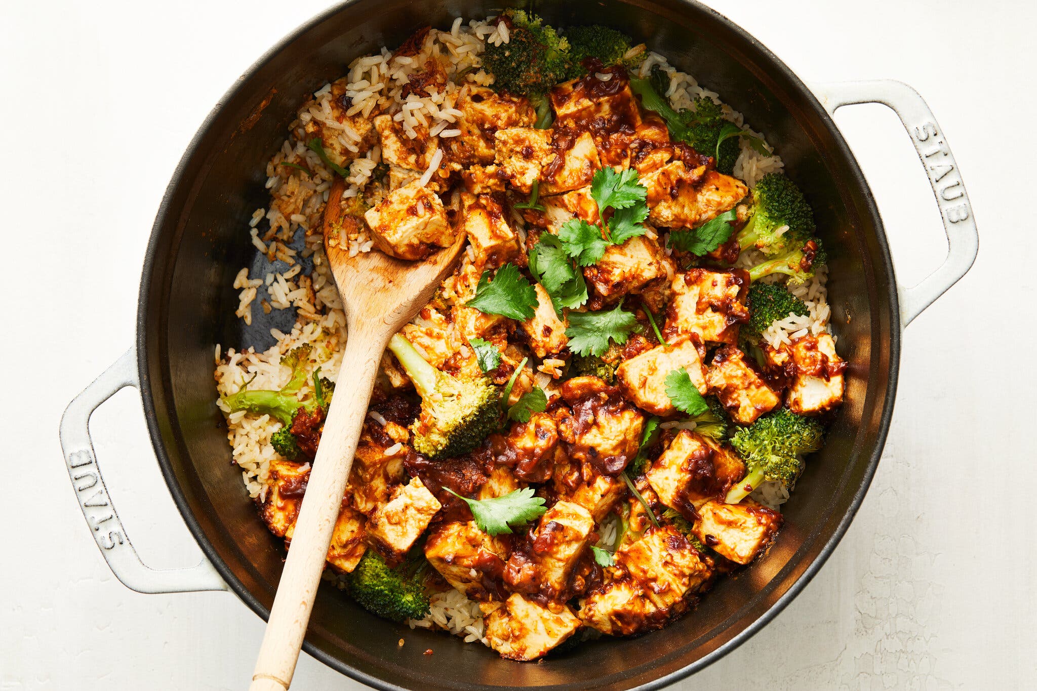 A Dutch oven is filled with rice, tofu, broccoli, chile sauce and cilantro.