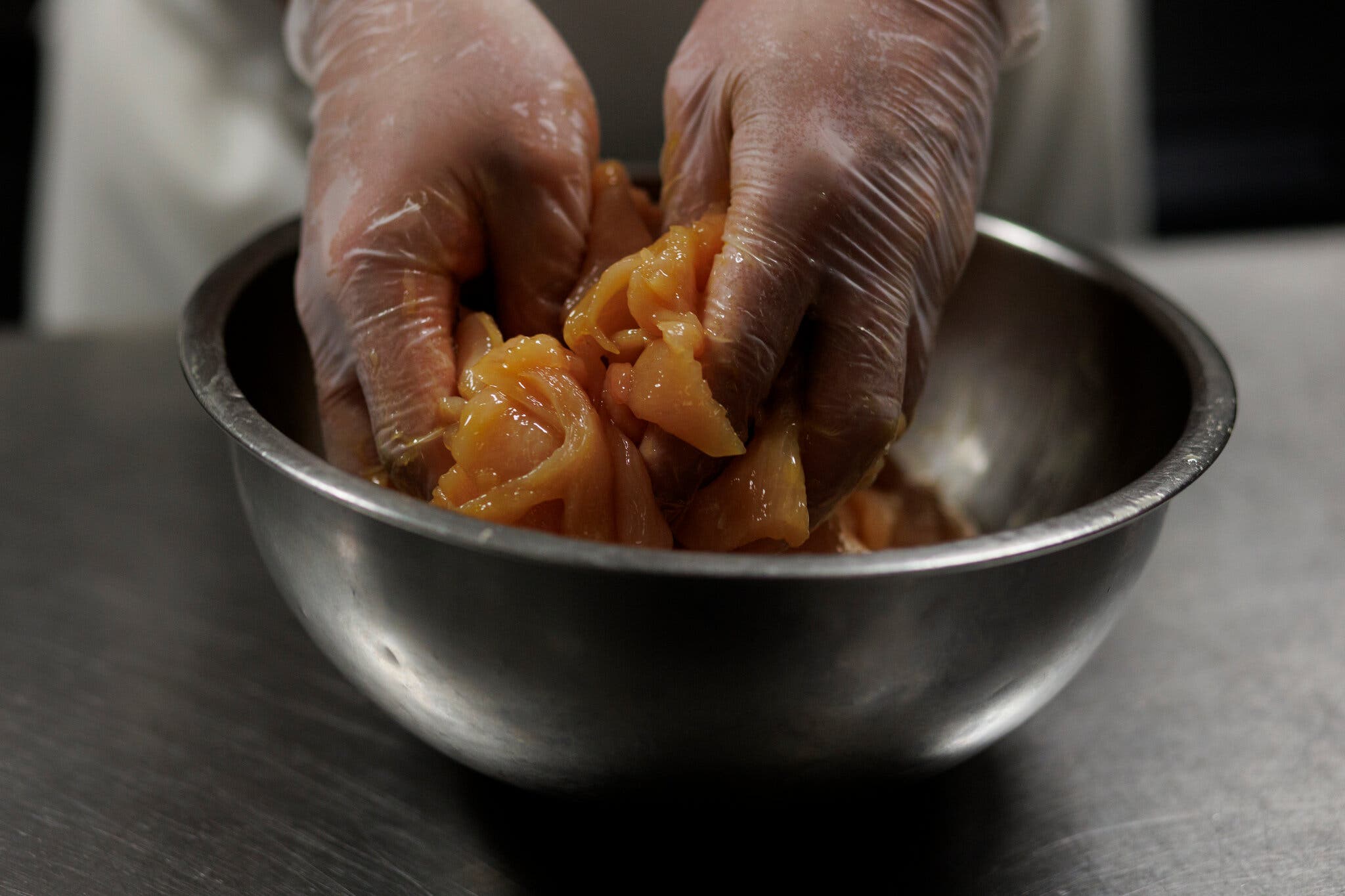 Two gloved hands massage chicken breast slices coated in marinade.