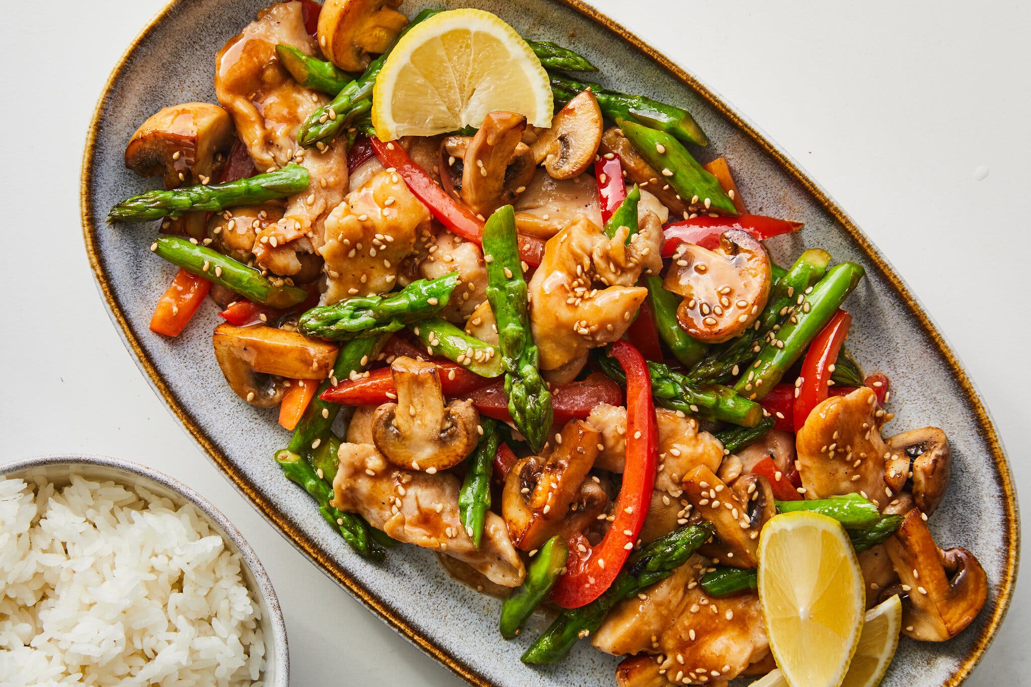 A platter holds a chicken stir-fry with asparagus, red pepper and mushrooms.